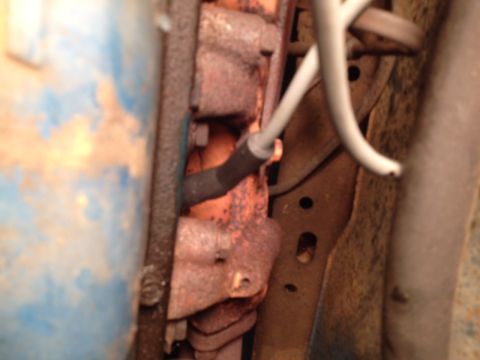 1973 Ford Bronco - Close-up of a corroded engine part with a blue painted surface and a grey wire.