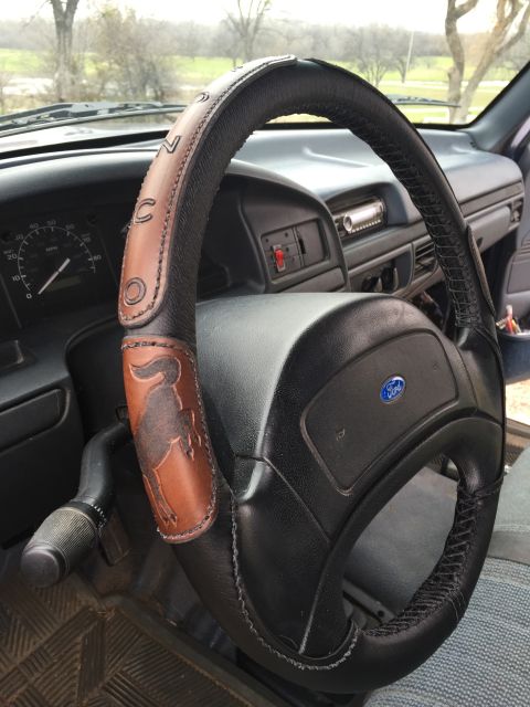 1993 Ford Bronco - The steering wheel of a 1993 Ford Bronco features a custom leather cover with a Bronco emblem and stitched lettering.