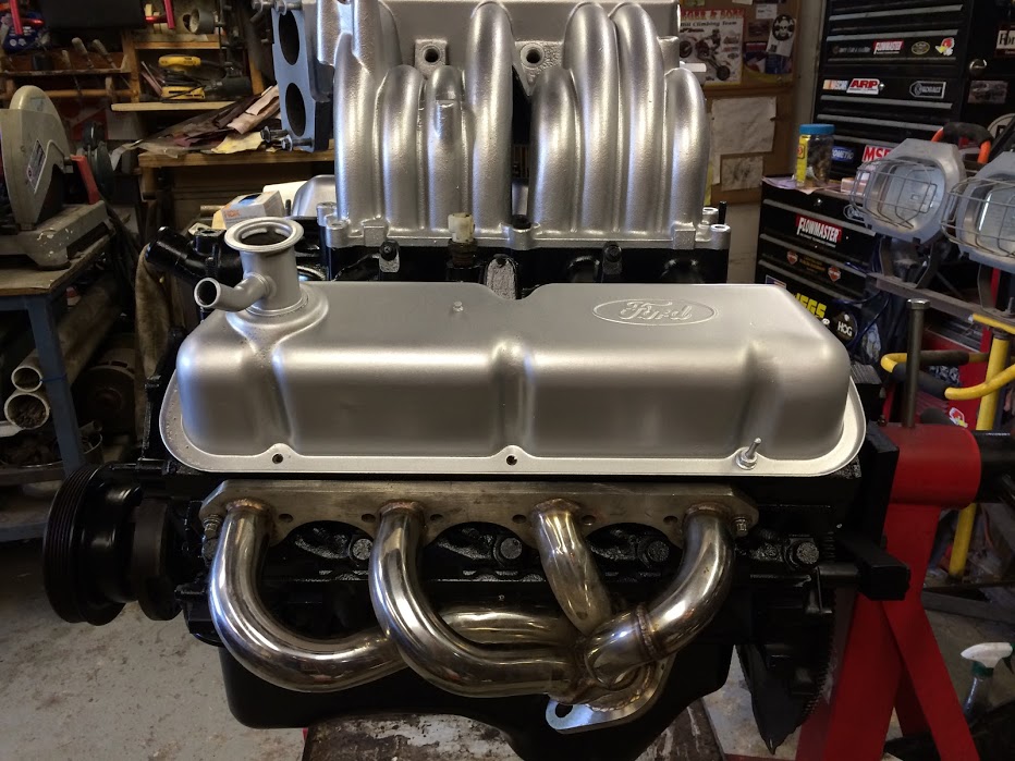 Silver Ford V8 engine with chrome headers on a red engine stand.
