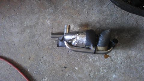 1994 Ford Bronco - A custom exhaust component, possibly a muffler or resonator, is shown lying on a concrete floor. It features stainless steel piping and a b…