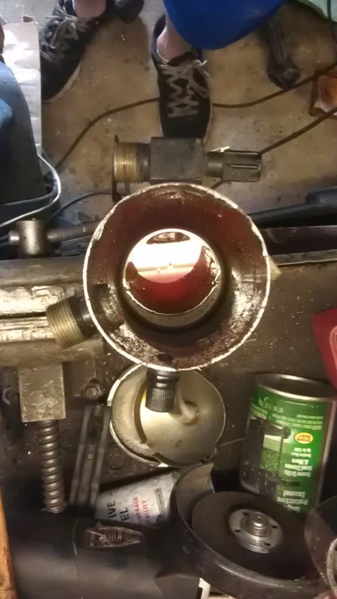 1994 Ford Bronco - A close-up view inside a metal cylinder containing a reddish-brown liquid, possibly oil or fuel. The cylinder has threaded fittings on the…