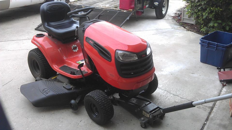 Red riding lawn mower on a jack in a driveway.
