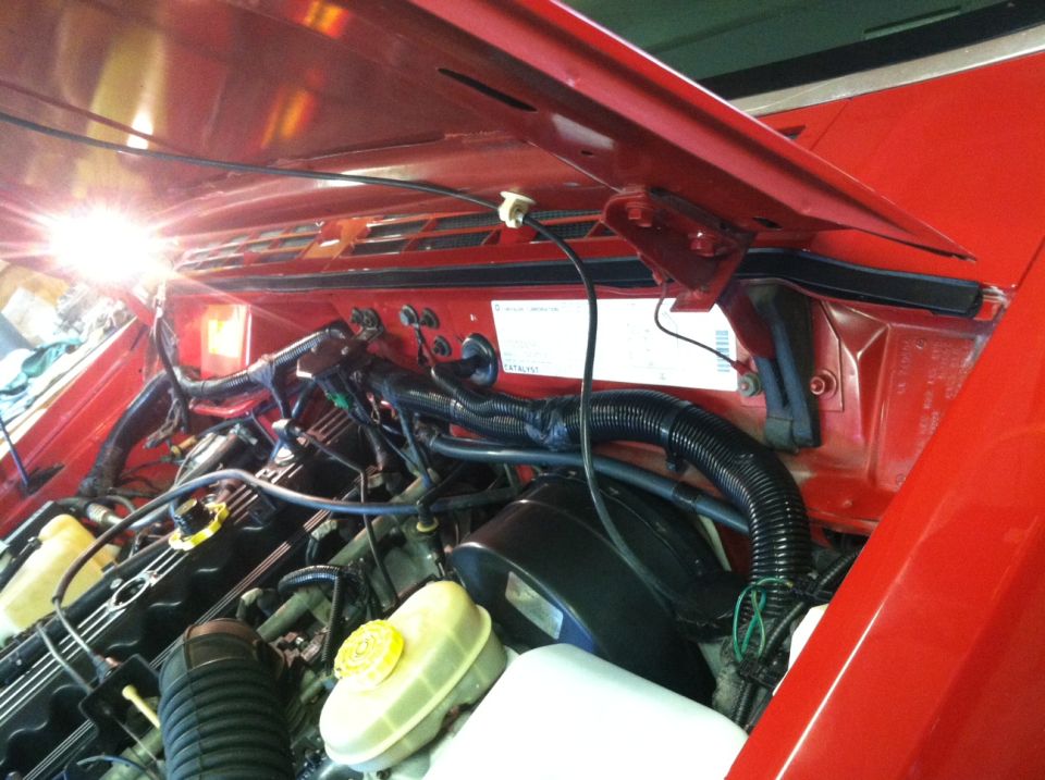 Red Jeep Comanche engine bay with hood open, showing engine components and wiring.