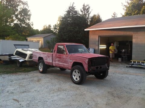 1991 Jeep Comanche - A red pickup truck from the 1980s is parked in a driveway next to a building.