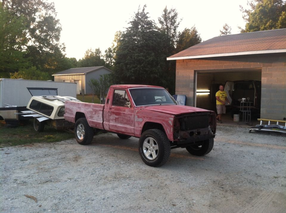 Red pickup truck, possibly 1980s model, parked outside a building with a trailer behind it