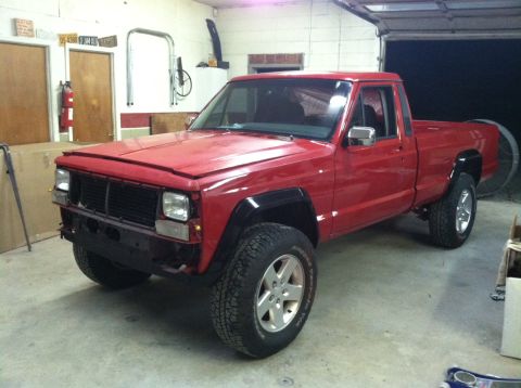 1991 Jeep Comanche - A red Jeep Comanche pickup truck is parked inside a garage with the hood up and front bumper removed.