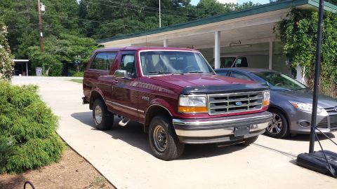 1993 Ford Bronco - A maroon 1993 Ford Bronco is parked on a concrete driveway next to a modern gray sedan.