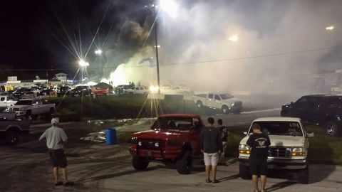 1995 Ford Bronco - A red Ford F-150 pickup truck is parked on a dirt track at night, with smoke billowing in the background from a drag racing event. Several…