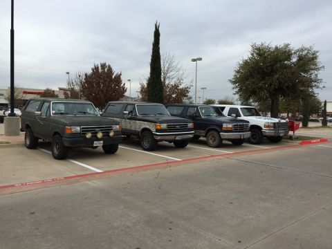 1993 Ford Bronco - A line of four Ford trucks and one Ford Bronco are parked in a parking lot under a cloudy sky. The vehicles are all facing to the right, wi…