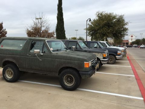 1993 Ford Bronco - A line of four Ford trucks, including a dark green Bronco in the foreground, are parked in a parking lot with a Target store in the backgro…