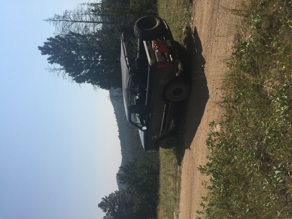 Off-road SUV parked on a dirt road with spare tire and jerry can on roof rack.