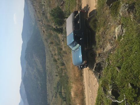 1994 Ford Bronco - A blue Ford Bronco is parked on a dirt road on a mountainside with steep slopes and sparse vegetation.