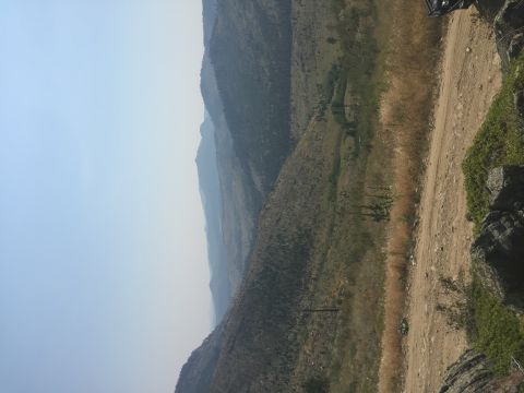 1994 Ford Bronco - A dirt road winds through a mountainous landscape under a hazy sky. The image is oriented vertically, showing a vast expanse of hills and v…