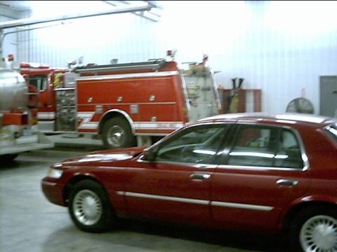2000 Mercury Grand Marquis - A red sedan is parked inside a garage, with a fire truck visible in the background.