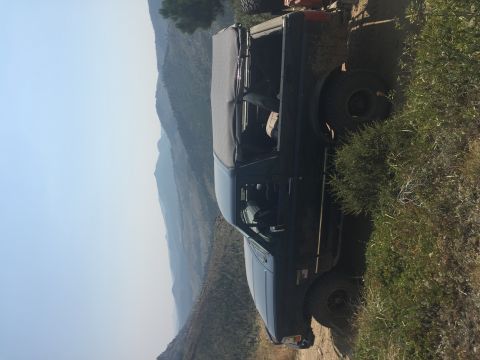 1994 Ford Bronco - A black Ford Bronco with a soft top is parked on a dirt road overlooking a mountainous landscape. The vehicle appears to be off-roading, wi…