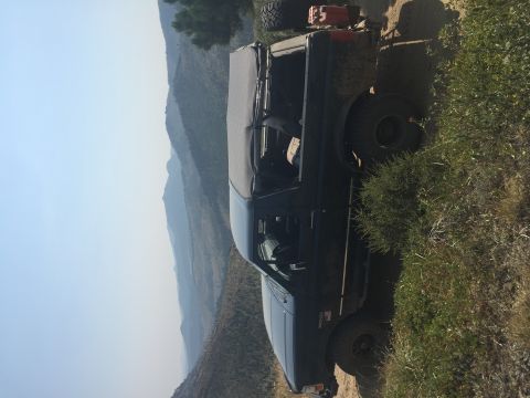 1994 Ford Bronco - A dark-colored Ford Bronco with a soft top is parked on a dirt road with a mountainous landscape in the background.