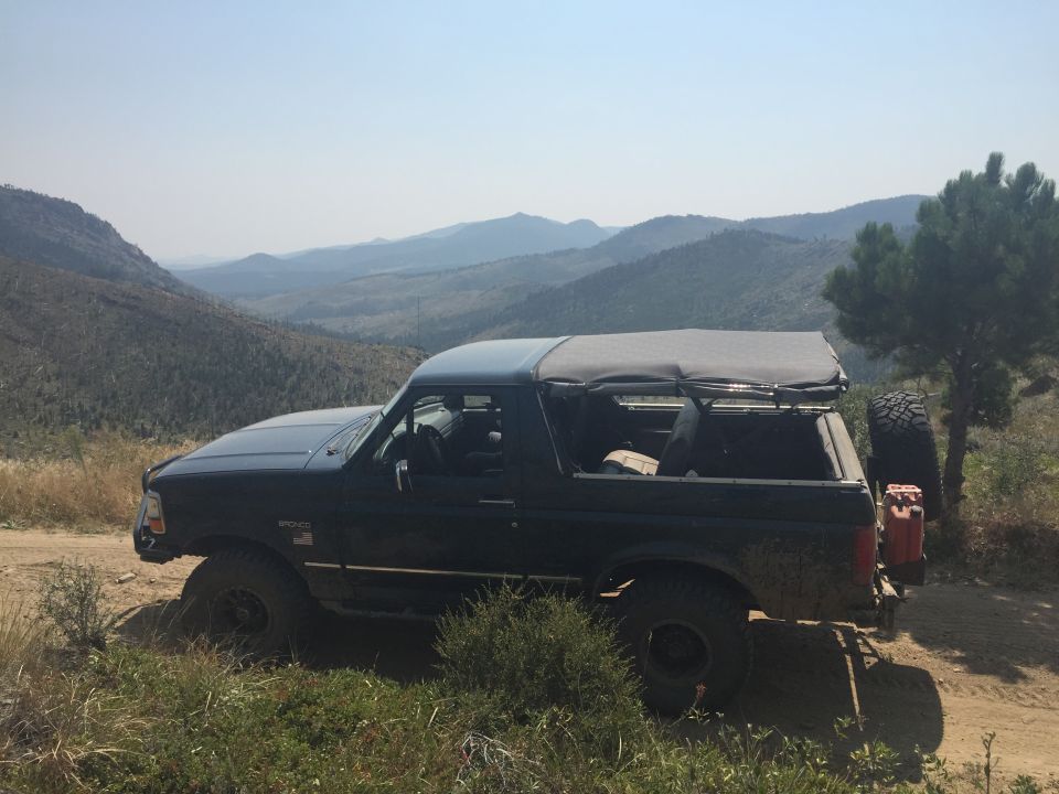 Dark 1994 Ford Bronco with soft top parked on dirt road, overlooking mountains.