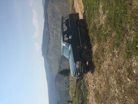 1994 Ford Bronco - A dark SUV is parked precariously on a steep, grassy slope overlooking a mountain range.