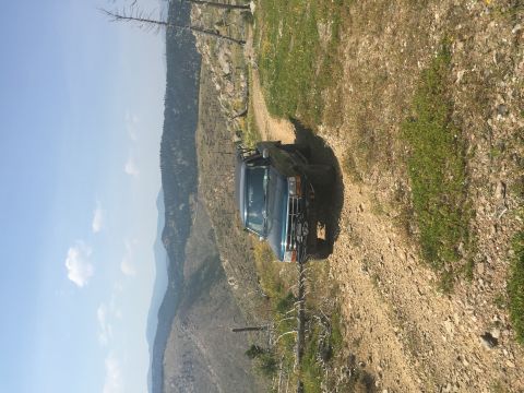 1994 Ford Bronco - A dark blue SUV navigates a dusty mountain road under a clear blue sky.