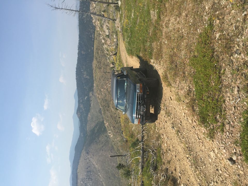 Dark blue SUV on a dirt road with mountains in the background. The vehicle has a snorkel and off-road tires