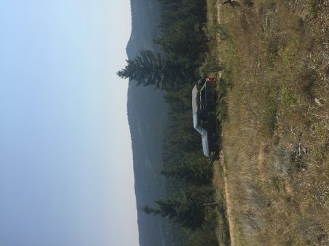 1994 Ford Bronco - A dark blue Ford Bronco is parked on a grassy hillside, with trees and mountains visible in the distance.