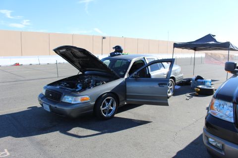 2003 Ford Crown Victoria - gray Ford Crown Victoria sedan sits with its hood up exposing the engine bay, doors open and a tent set up beside it in a sunny lot.