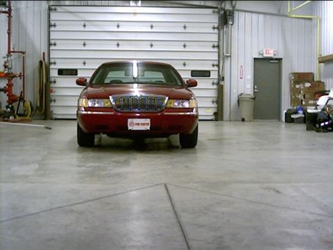 2000 Mercury Grand Marquis - A red 2000 Mercury Grand Marquis is parked in front of a large garage door.