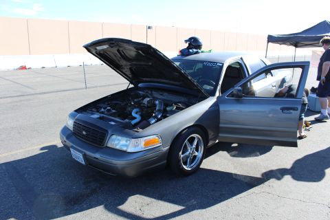 2003 Ford Crown Victoria - gray Ford Crown Victoria sits hood-up showing its engine bay while people work at the open passenger door under a canopy in a lot.