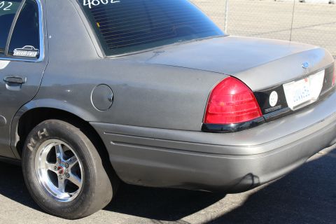 2003 Ford Crown Victoria - Close rear-quarter view of a gray Ford sedan fitted with a chrome wheel and drag slick tire, tail light and fuel door in frame.