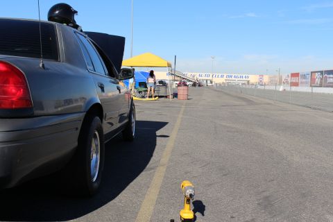 2003 Ford Crown Victoria - Rear-quarter view of a gray sedan along the Auto Club Dragway lane with a yellow cordless drill on the pavement and a tent in the distance.