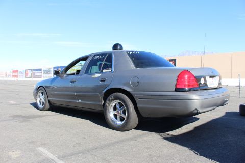 2003 Ford Crown Victoria - gray Ford Crown Victoria sedan with drag wheels and tires sits on a sunlit lot, taillight glowing, mountains in the distance.