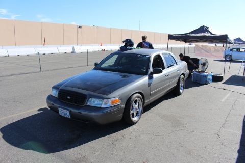2003 Ford Crown Victoria - gray Ford Crown Victoria sits at an outdoor motorsport event with pop-up tents, cones and spectators in the background.