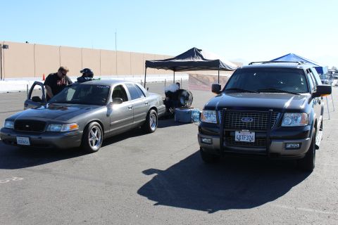 2003 Ford Crown Victoria - gray Ford Crown Victoria with its driver door open sits beside a black Ford Expedition under canopy tents on a parking lot.
