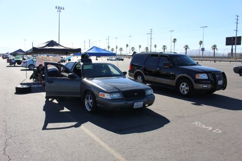 2003 Ford Crown Victoria - gray Ford Crown Victoria with door ajar parks near a black Ford Expedition amid tents, palm trees and stadium lights.
