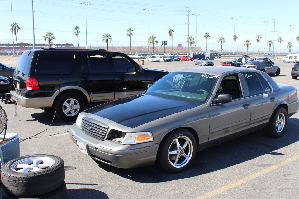 Front left view of a gray Ford Crown Victoria with a spare wheel and tire on the ground
