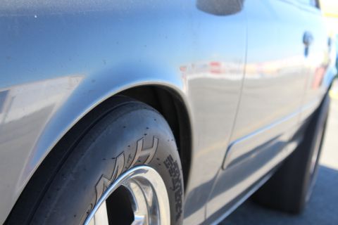 2003 Ford Crown Victoria - Close-up of a silver-gray car's rear fender and polished wheel wrapped in an M&H drag-radial tire on asphalt.