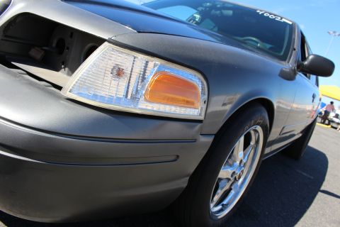 2003 Ford Crown Victoria - low-angle close-up of a gray Crown Victoria's clear headlight assembly, amber turn signal and chrome front wheel.