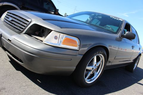 2003 Ford Crown Victoria - low-angle shot of a gray Ford Crown Victoria with hood ajar, showing its grille, headlight and chrome drag wheel.