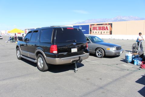 2003 Ford Crown Victoria - black Ford Expedition Eddie Bauer SUV with a tow ball is parked beside a gray sedan, a Bubba Burger sign on the building behind.