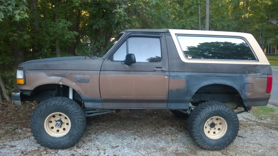 1992 Ford Bronco, lifted with large off-road tires, side view. Paint is worn