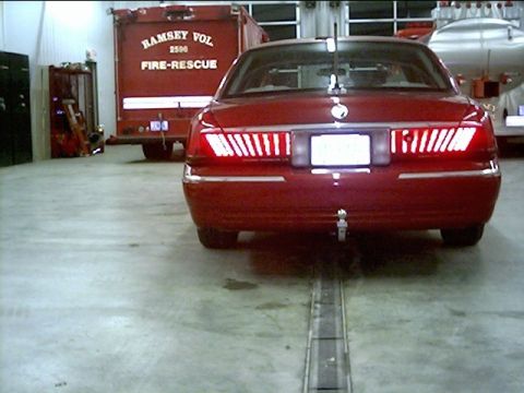2000 Mercury Grand Marquis - Rear view of a red 2000 Mercury Grand Marquis parked inside a firehouse next to a fire truck.