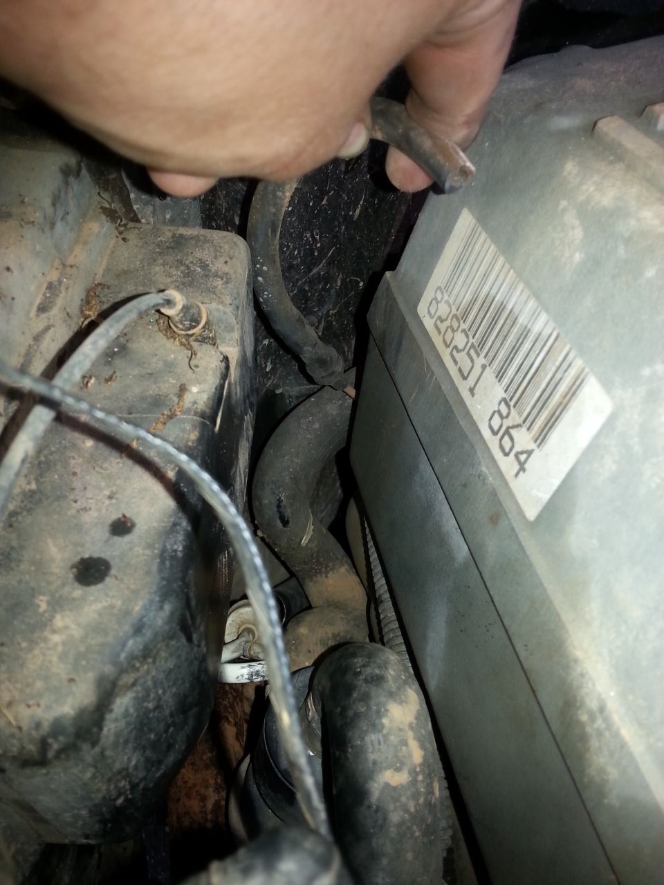 Close-up of engine bay with hoses and a gray box with a barcode and numbers 828251 864