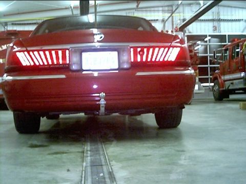 2000 Mercury Grand Marquis - Rear view of a red 2000 Mercury Grand Marquis with a trailer hitch, parked indoors near a fire truck.