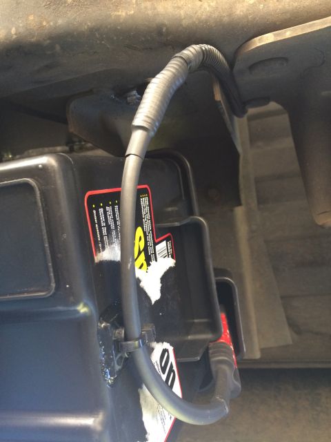 1997 Dodge 3500 - A black battery with red and yellow labels is secured under a vehicle, with a flexible conduit protecting its wiring.