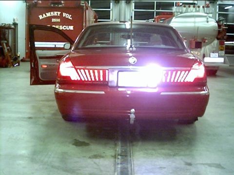 2000 Mercury Grand Marquis - A red sedan is parked inside a garage with its driver's door ajar and bright taillights illuminated.