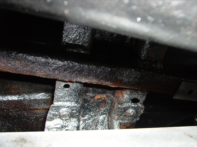 Undercarriage frame with rust and black undercoating. Visible bolts and mounting brackets
