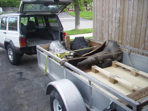 1978 Ford Bronco - A Jeep Cherokee is parked next to a trailer carrying transmission components.