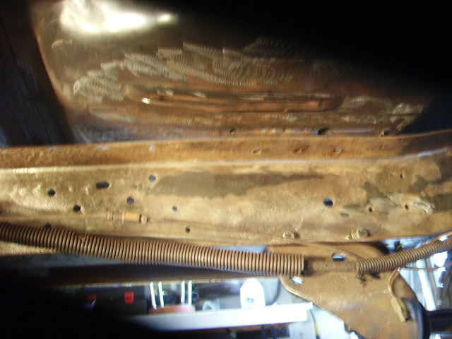 Close-up of a rusted metal frame with a coiled spring and wiring harness, showing signs of wear and repair