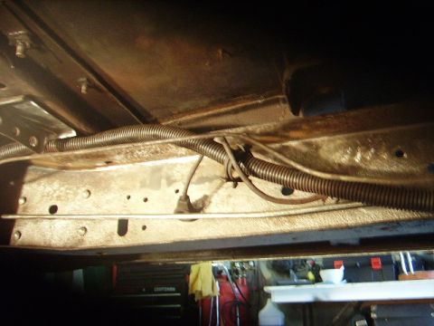 1978 Ford Bronco - The undercarriage of a vehicle shows various wires and protective conduit running along the frame.