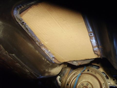 1978 Ford Bronco - The underside of a vehicle shows a transmission bell housing and a makeshift patch made of cardboard.
